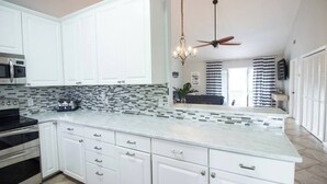 A kitchen with white cabinets, a tiled backsplash, a built-in oven, and a ceiling fan. - Stay a While - 3 min walk to private beach access!

 (Destin)