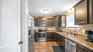 A modern kitchen with dark wood cabinets, stainless steel appliances, granite countertops, and a tiled backsplash. - Serene Retreat Near Fort Campbell and Casino -  Family and Pet Friendly (Clarksville)