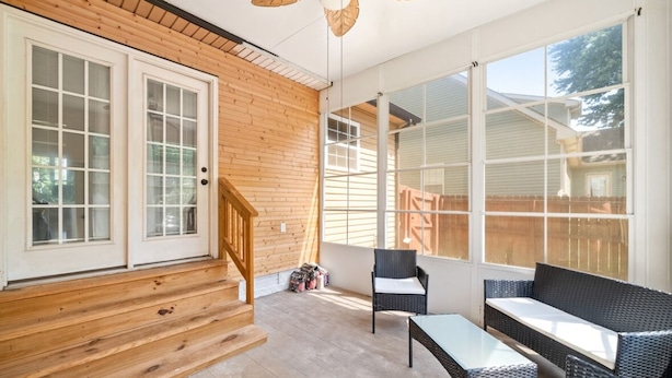 A sunlit room with wooden walls, large windows, a staircase, and wicker furniture. - Serene Retreat Near Fort Campbell and Casino -  Family and Pet Friendly (Clarksville)
