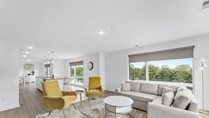Amplia sala de estar con sofá, sillones y una mesa de centro. Se aprecia un ventanal con vista a zonas verdes.