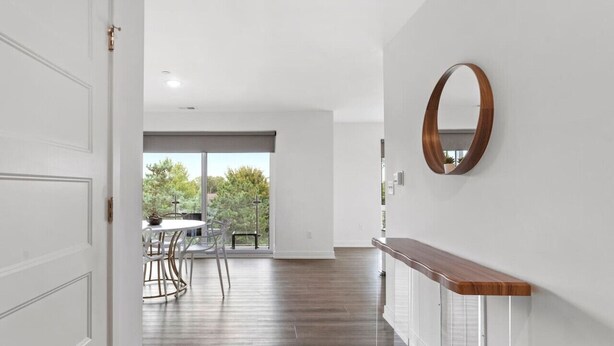 Un interior moderno con piso de madera, paredes blancas, un espejo redondo y una zona de comedor con sillas y una mesa.