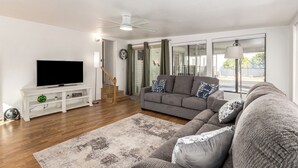 A modern living room with a flat-screen TV, grey sofas, a white entertainment unit, and a staircase leading to another level. - Recliners! Large Az Room - Adult 55+ Activities Galore! (Mesa)