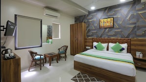 A hotel room with a bed, two chairs, a desk, a wardrobe, and a television. - hotel hi life DX (New Delhi)