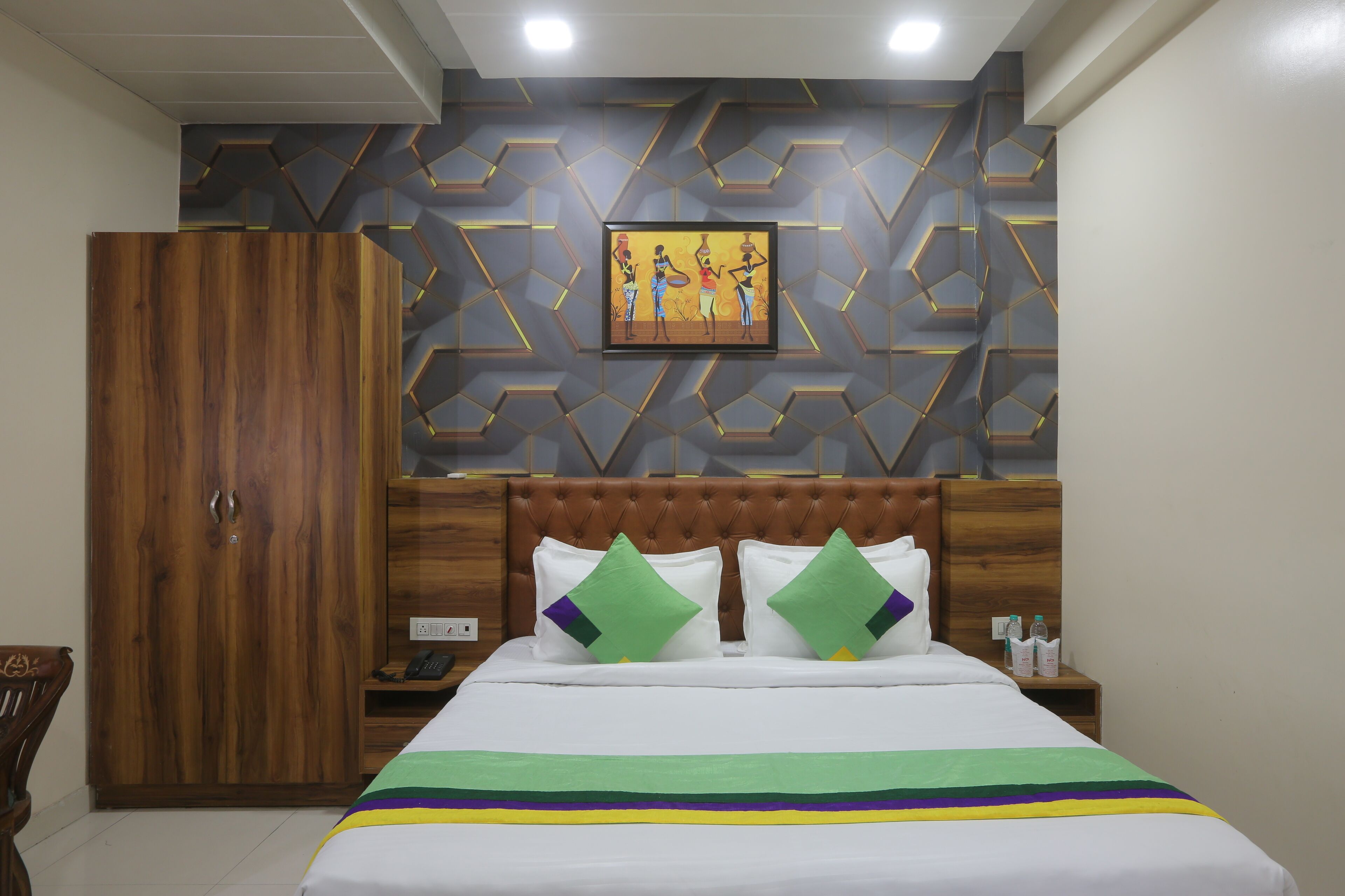 A hotel room with a bed, wooden wardrobe, and a geometric-patterned wall.