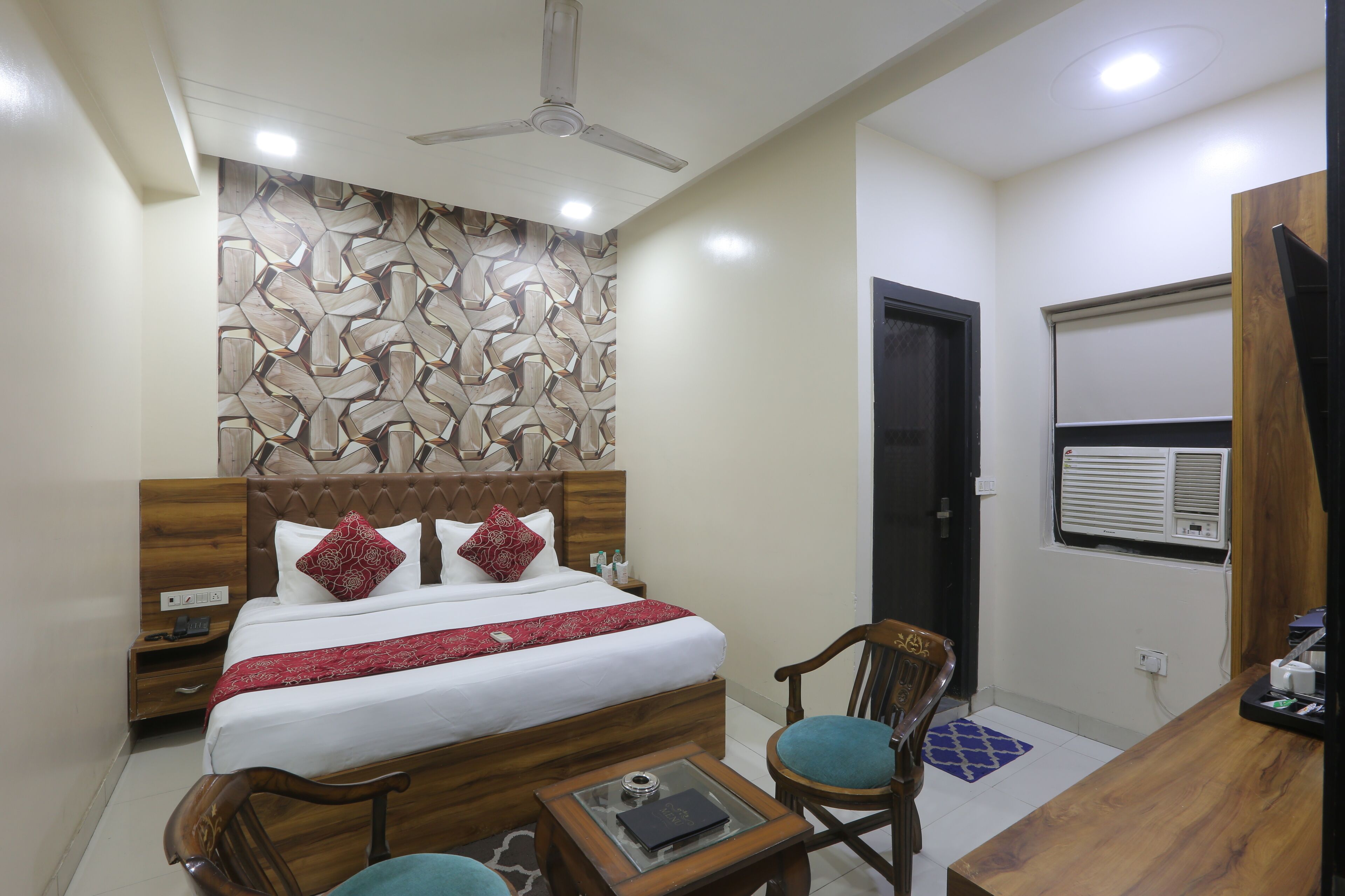 Una habitación de hotel con cama, mesita de noche de madera, escritorio, silla y ventilador de techo.