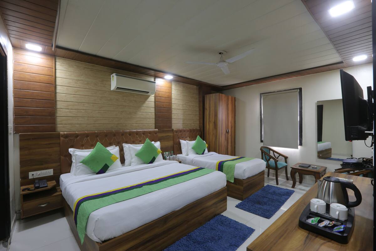A hotel room with two beds, a desk, a chair, a coffee maker, and a TV.