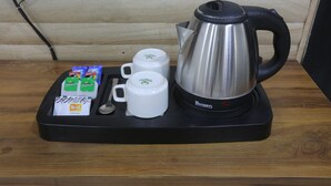 A coffee station with a stainless steel kettle, two white mugs, and packets of coffee creamer. - hotel hi life DX (New Delhi)