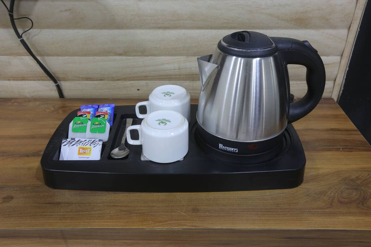 A coffee station with a stainless steel kettle, two white mugs, and packets of coffee creamer.