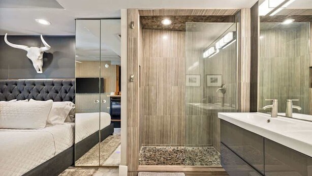 Ein modernes Schlafzimmer mit einem großen Bett, einer Dusche mit Glastrennwand und einem Schminktisch mit Spiegel.