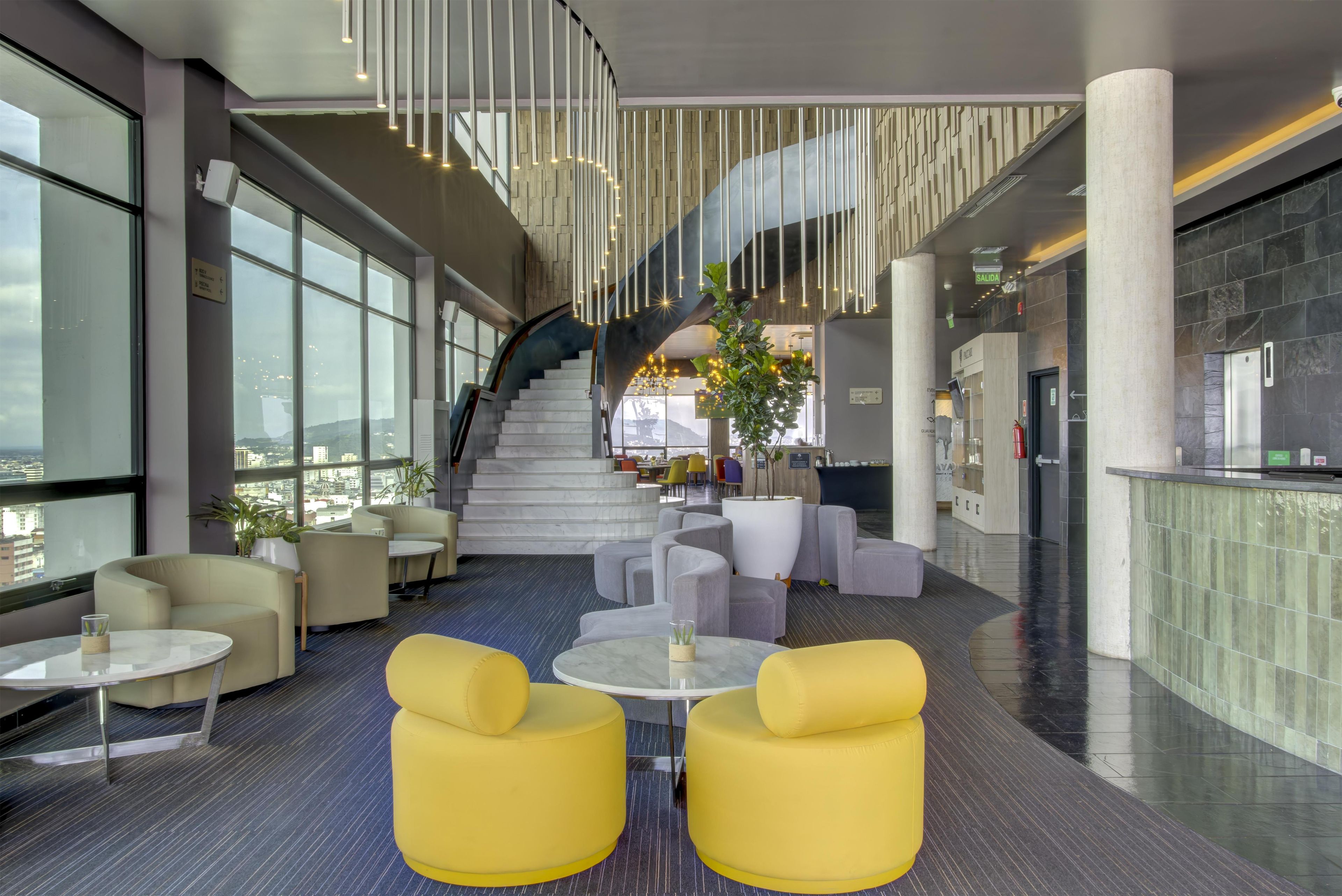 A modern lobby with a staircase, seating areas, and a view of the city.