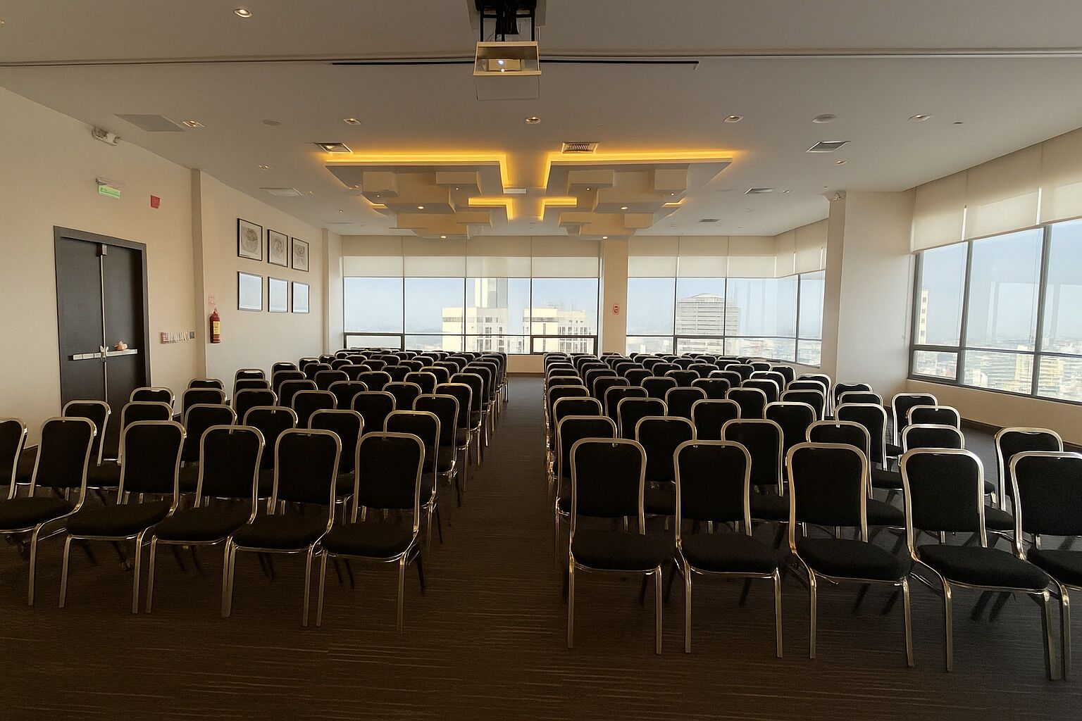 Een vergaderzaal met rijen stoelen, grote ramen en een modern plafond.