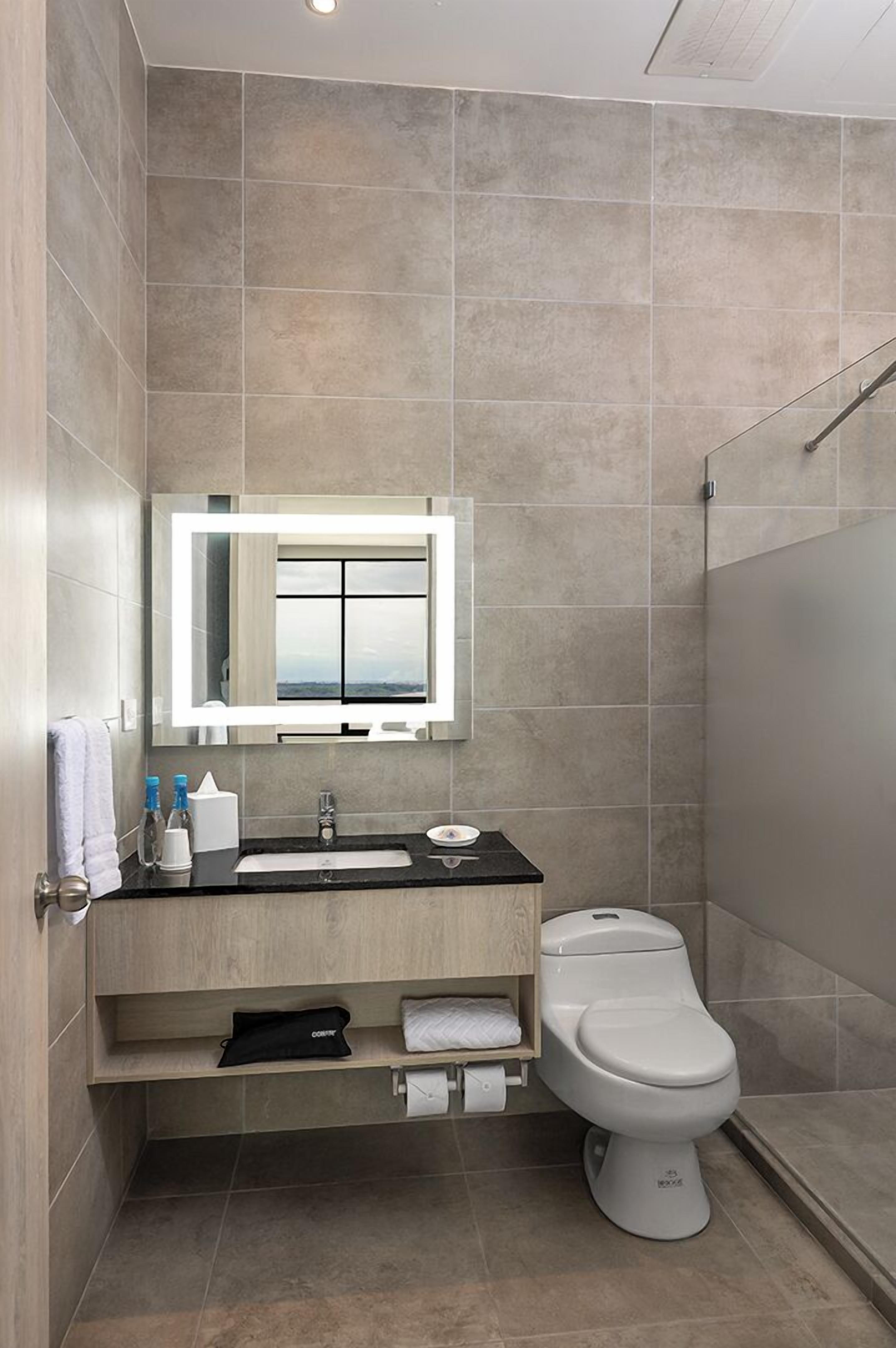 A modern bathroom with a large mirror, a sink, a toilet, and a shower area.