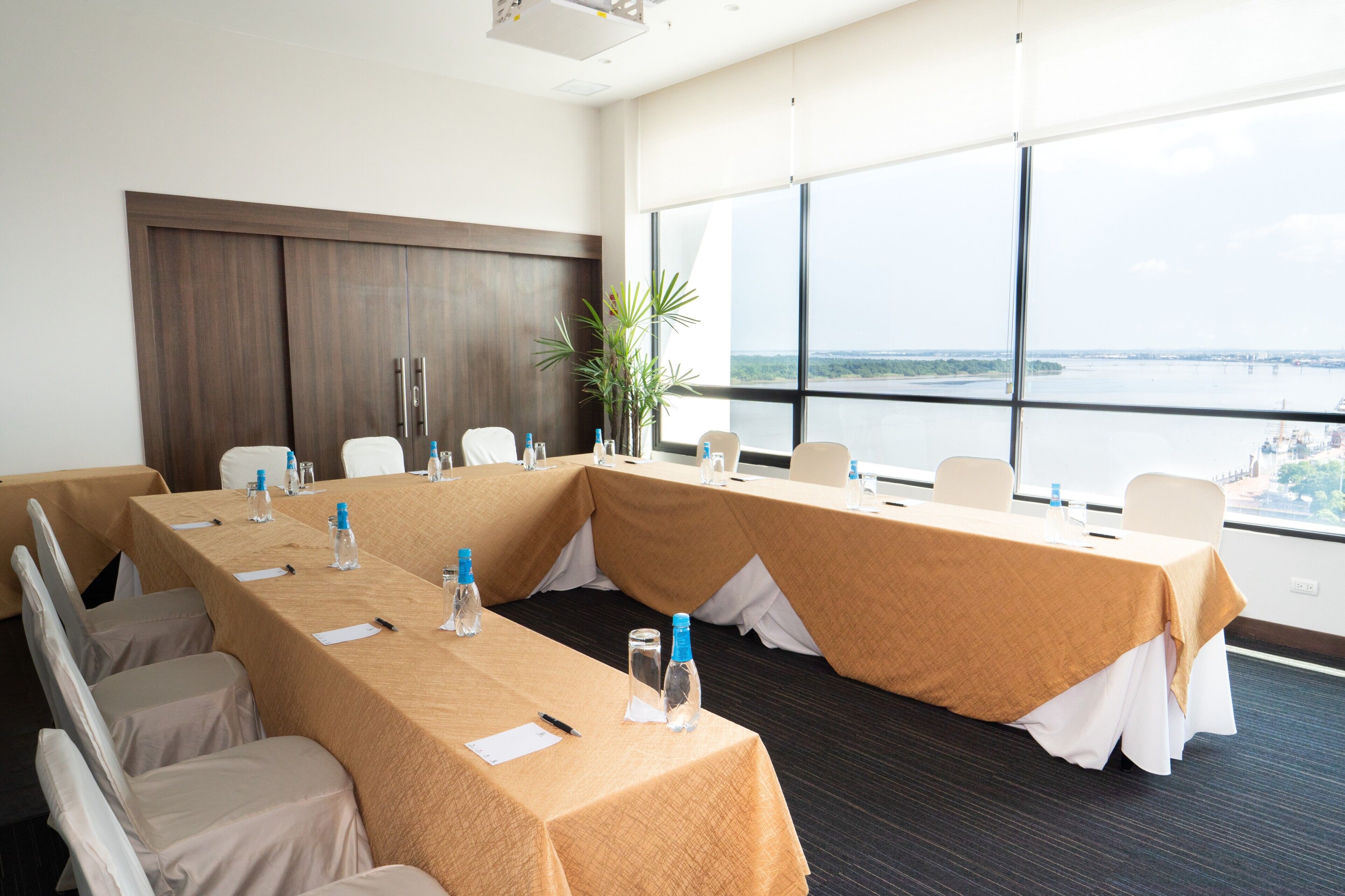 Un salón de conferencias con una mesa larga, sillas y vistas a una masa de agua a través de amplios ventanales.