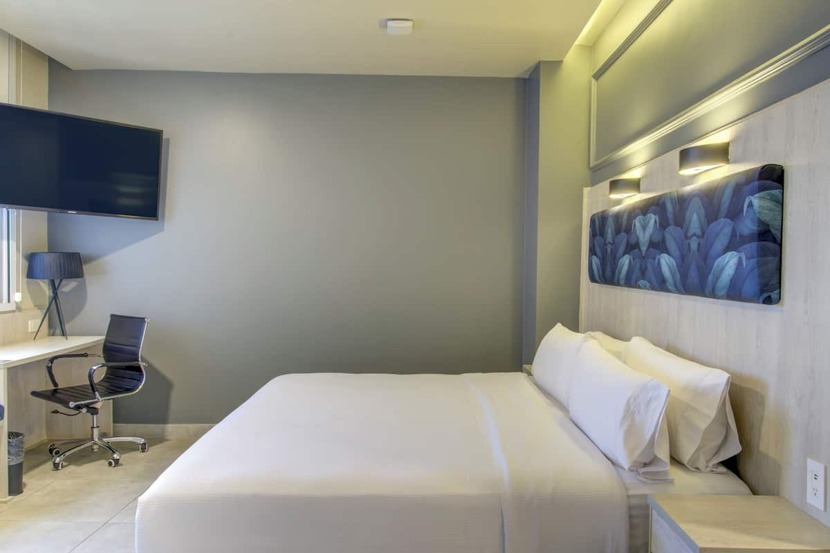 Ein modernes Hotelzimmer mit einem großen Bett, einem Schreibtisch mit Stuhl, einem flachbildfernseher an der Wand und einer Wanddekoration.