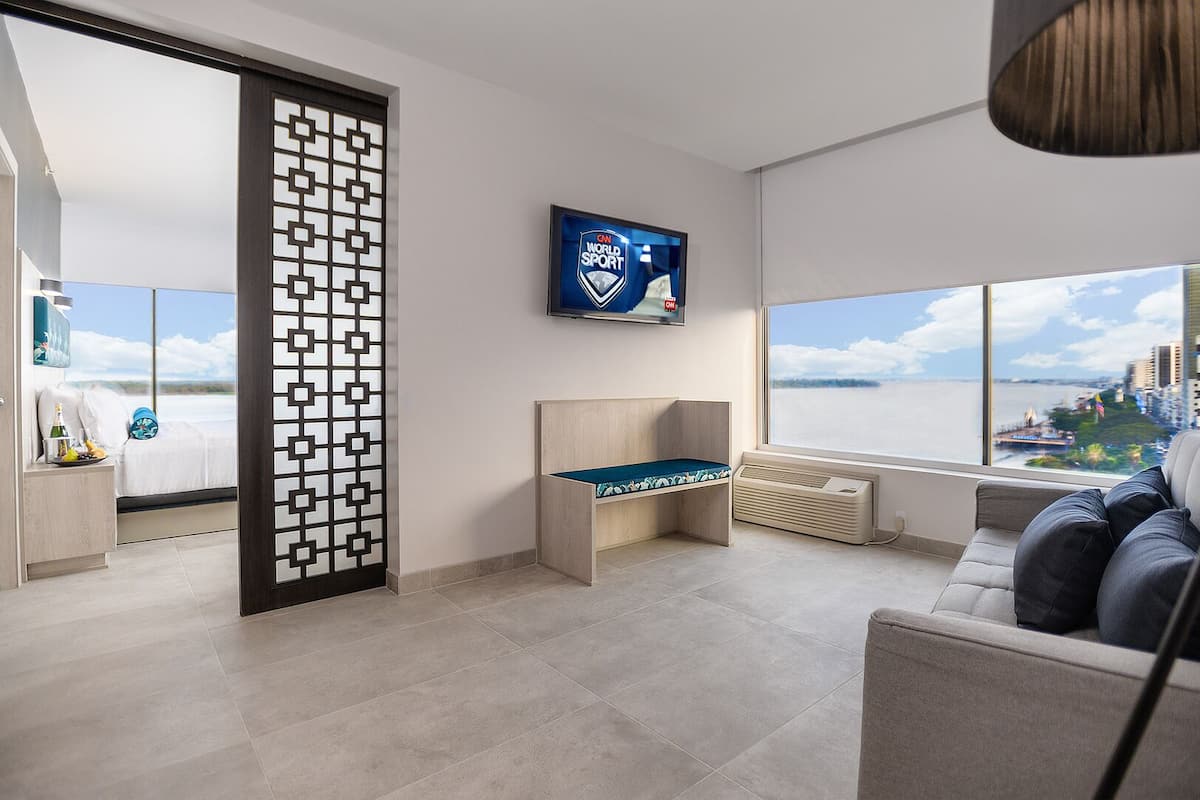 Ein modernes Hotelzimmer mit großem Fenster, Fernseher, Sofa und einer dekorativen Trennwand.