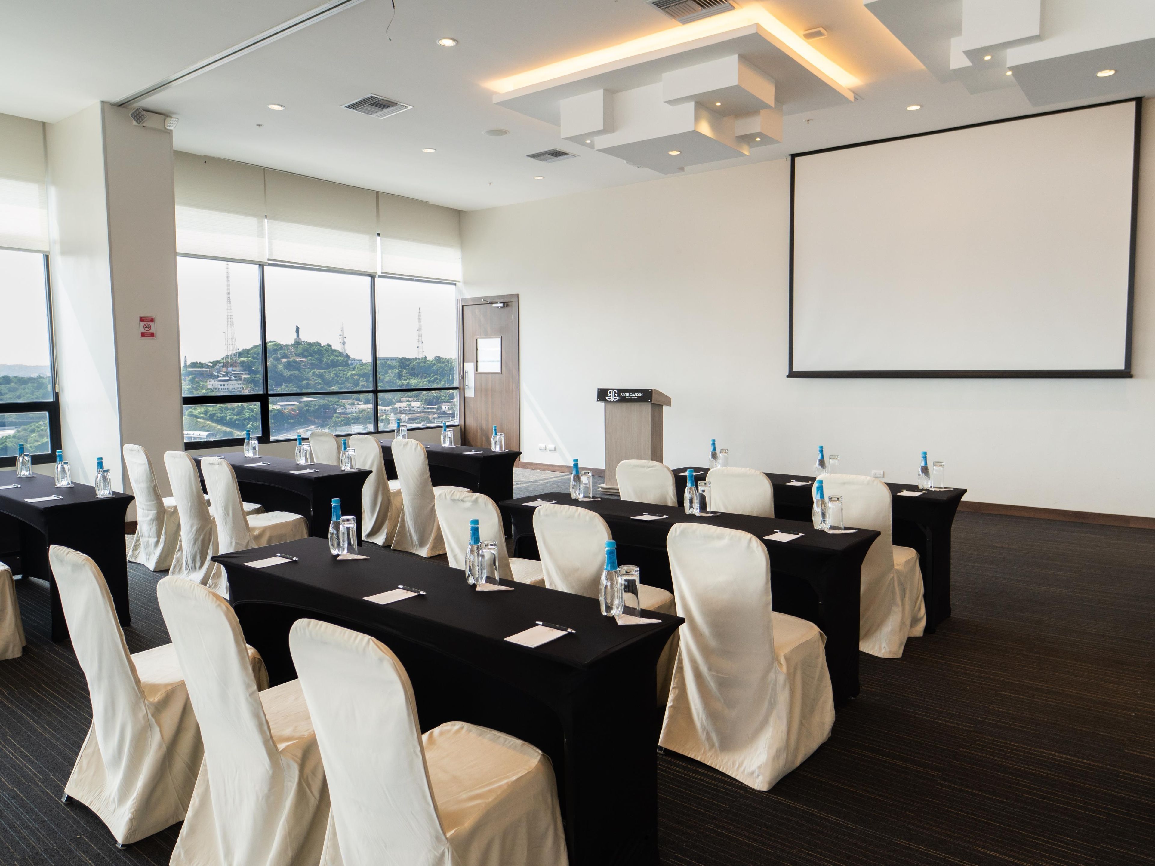 Una sala conferenze con tavoli, sedie e uno schermo per proiezioni.