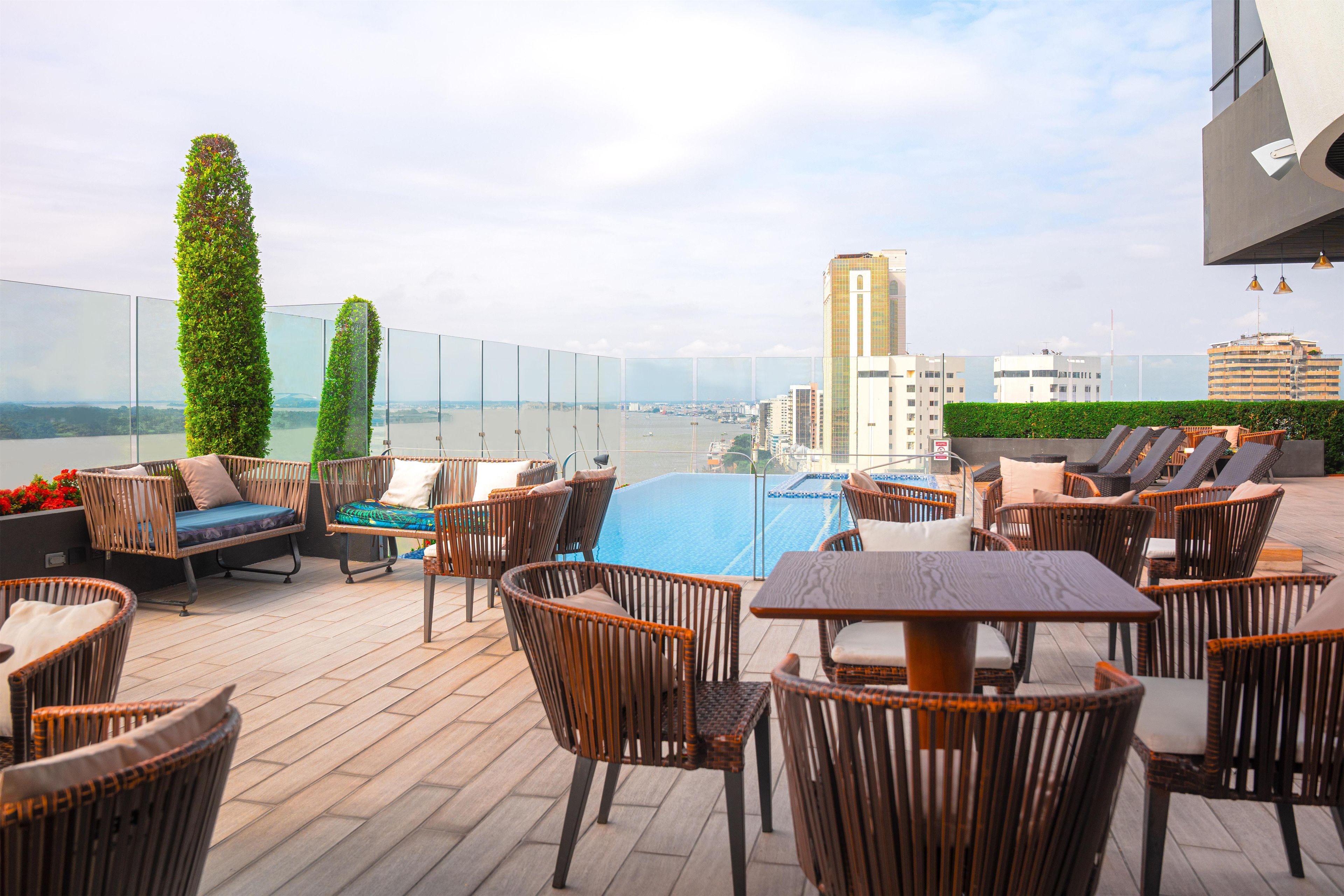 Una terraza en la azotea con piscina, sillones de descanso y vistas a la ciudad.