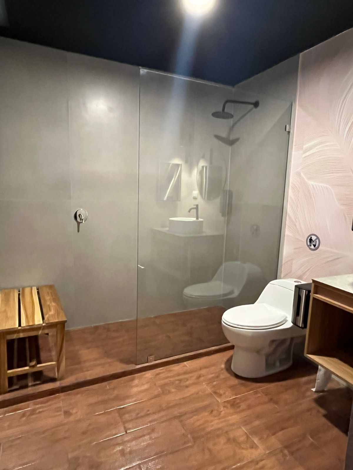 A modern bathroom with a glass-enclosed shower, a wooden vanity, and a white toilet.