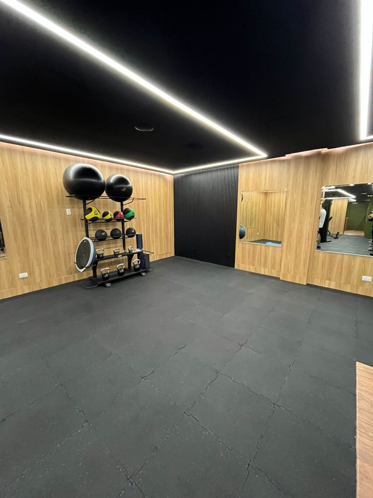 A gym with wooden walls, black rubber flooring, and various exercise equipment including kettlebells and medicine balls.