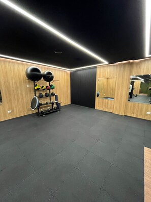 Et træningscenter med træpaneler, sort gummigulv og forskelligt træningsudstyr, herunder kettlebells og medicinbolde.