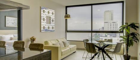 Una sala de estar moderna con sofá, mesa de comedor, sillas y un ventanal con vista a la ciudad.