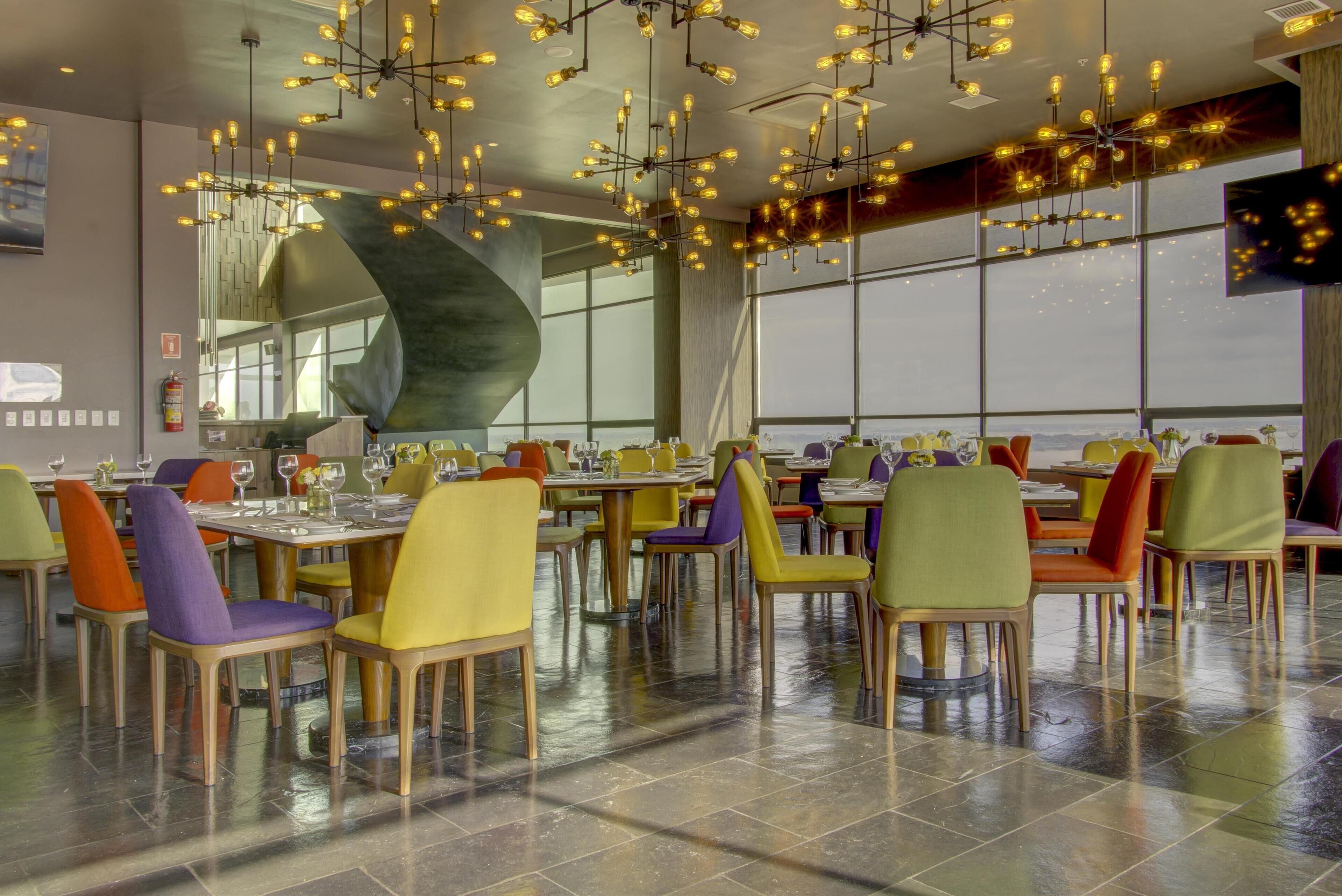 Un comedor moderno con varias mesas y sillas, ventanas amplias e iluminación contemporánea.