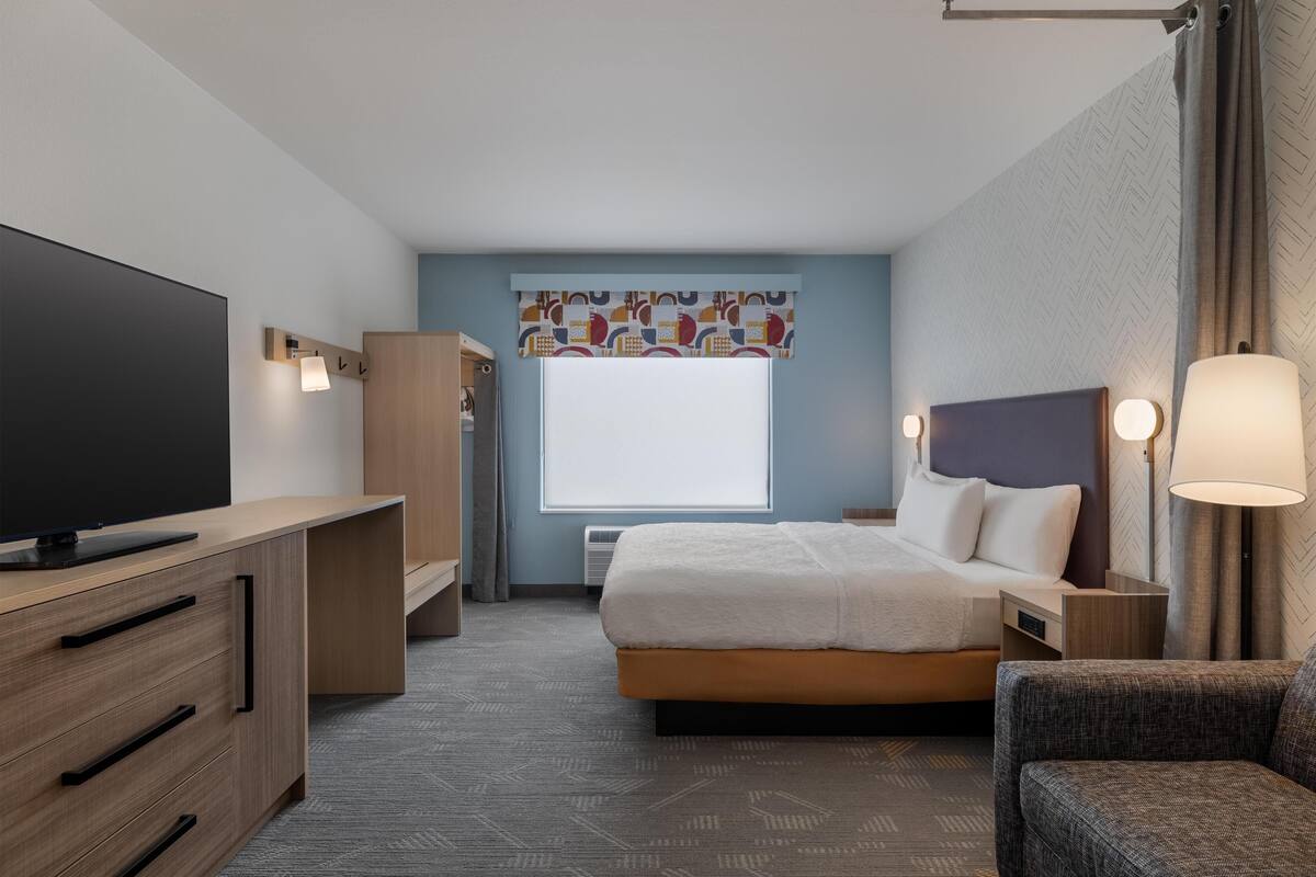 A hotel room with a bed, a TV, a desk, and a chair.