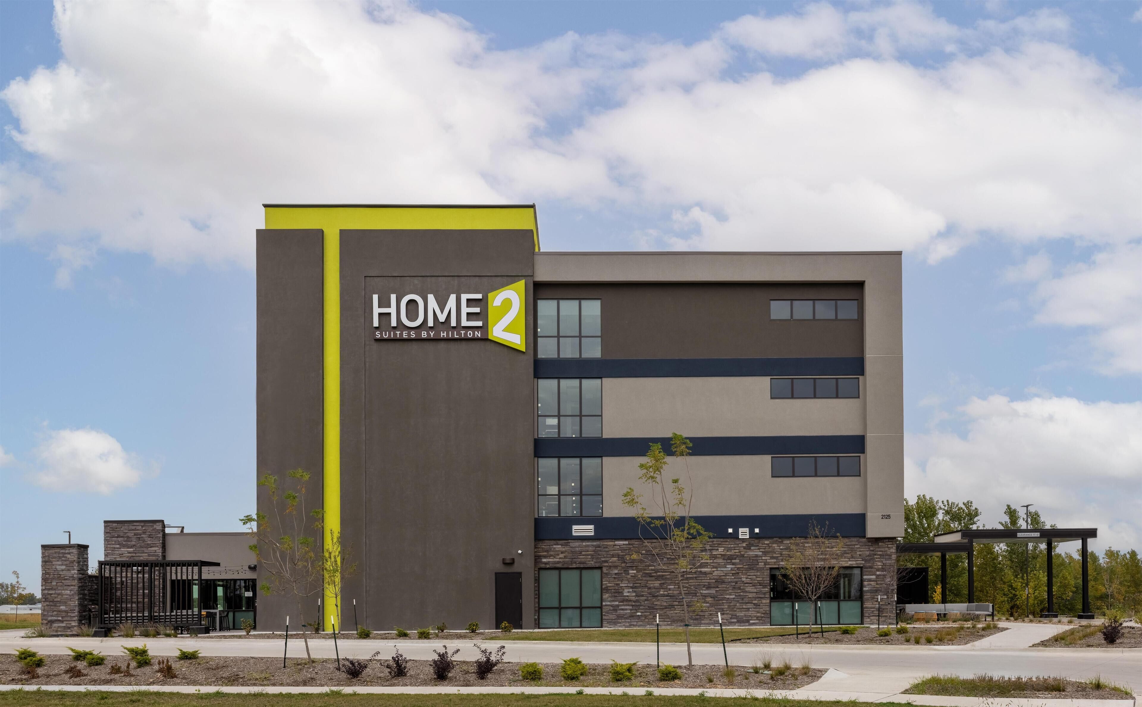 A modern hotel building with a sign reading "HOME 2 Suites by Hilton" and a number "2125" on the facade.
