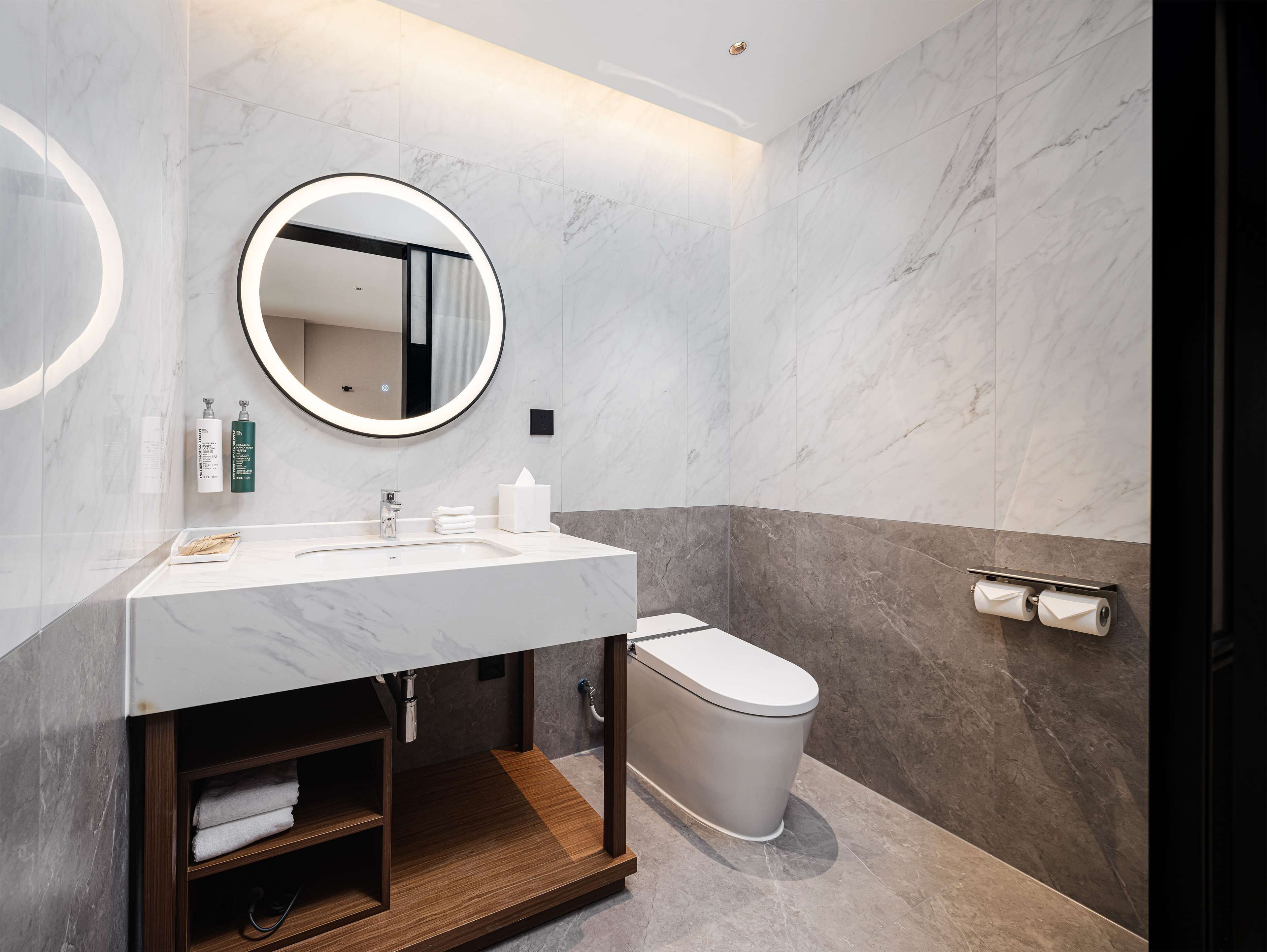 A modern bathroom with a marble vanity, a round mirror, a toilet, and a towel rack.