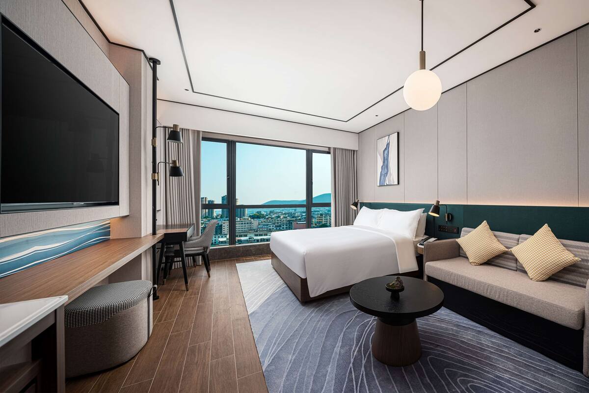 A modern hotel room with a large bed, a sofa, a desk, and a television.