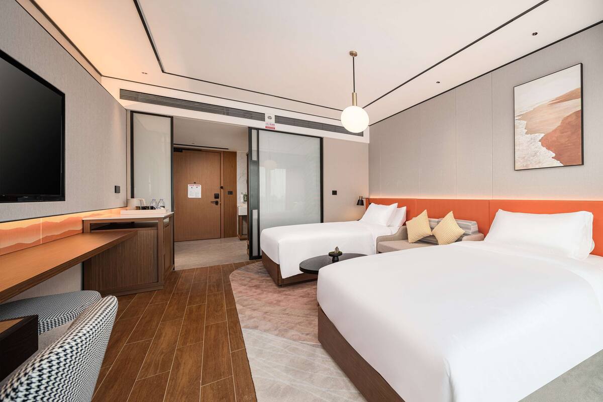 A modern hotel room with a large bed, a desk, a TV, and a bathroom.