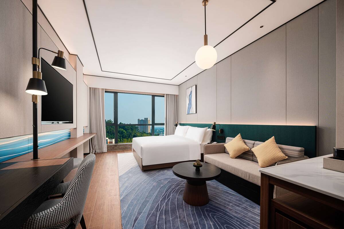 A modern hotel room with a large bed, a sofa, a dining table, and a TV.