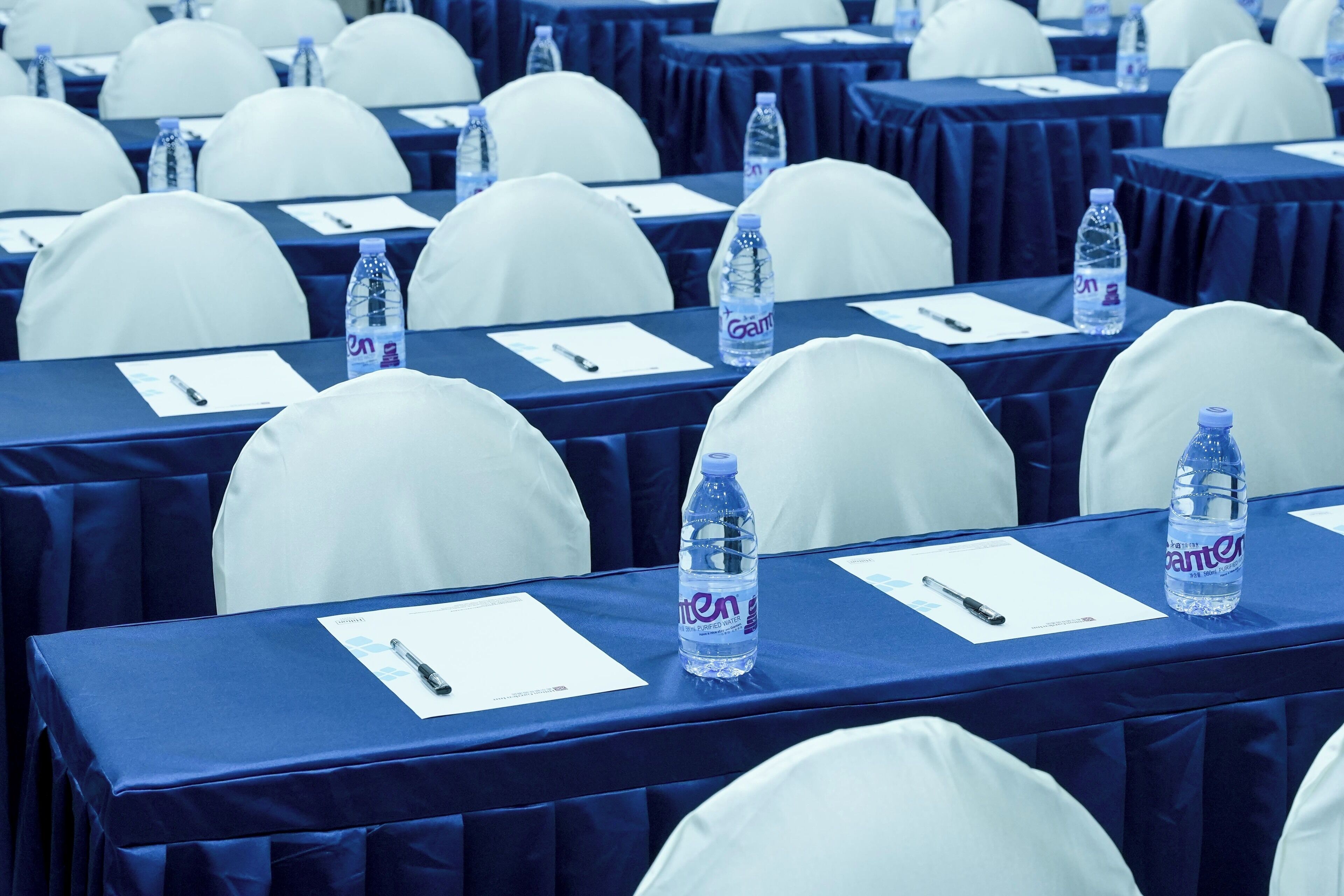 A conference room with rows of tables, each with a water bottle and a pen on a notepad.