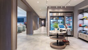 A modern hotel lobby with a seating area, a self-service kiosk, and a refrigerated display case. - Home2 Suites By Hilton Boone (Boone)