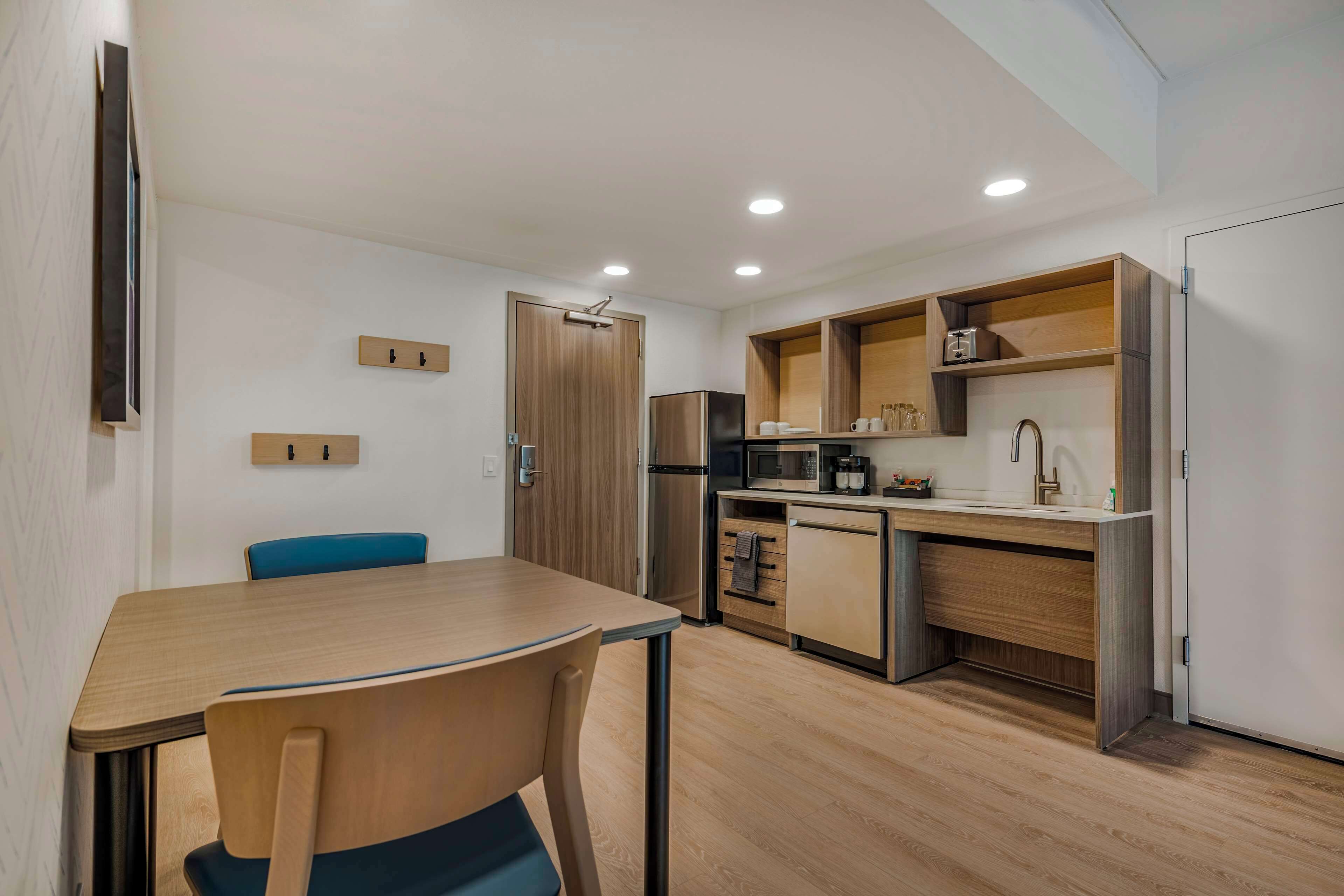 A compact kitchen with a dining area, wooden cabinets, a microwave, and a refrigerator.
