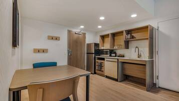 A compact kitchen with a dining area, wooden cabinets, a microwave, and a refrigerator.