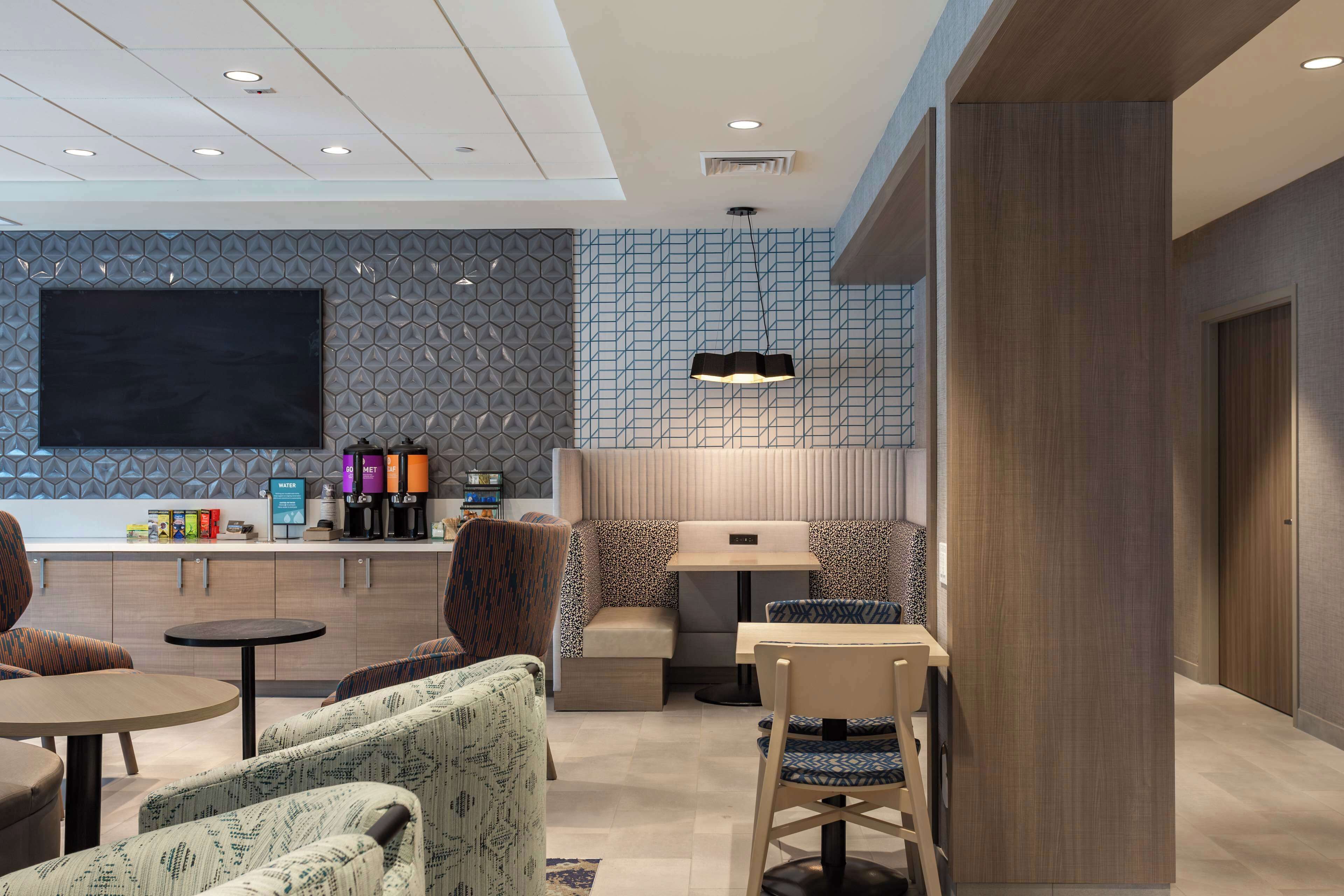 A modern hotel lobby with a seating area, a flat-screen TV, and a coffee station.