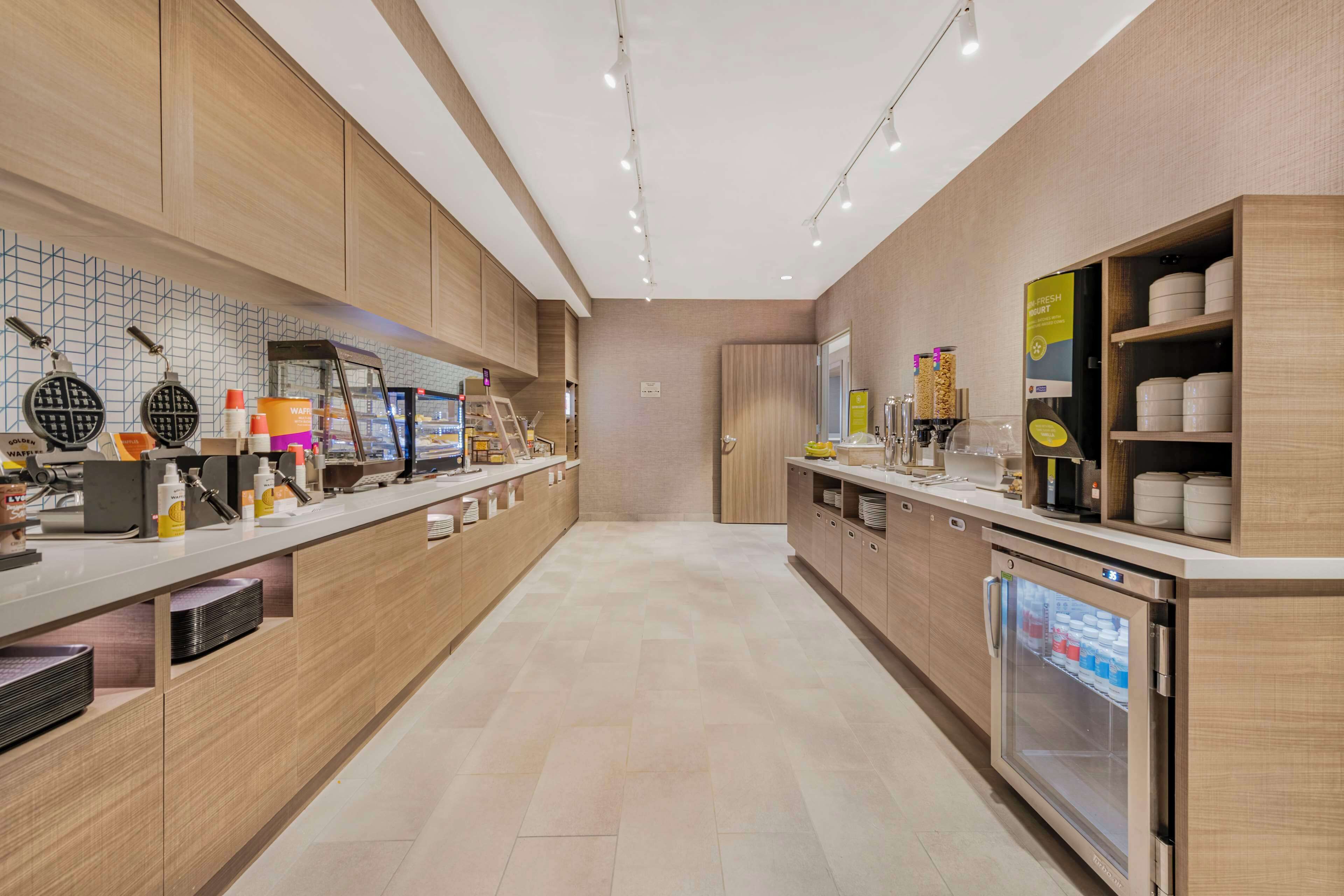 A modern kitchen with a long counter, waffle maker, coffee machine, and a refrigerator.