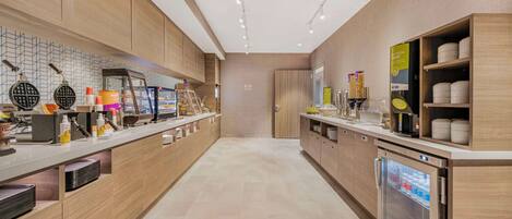 A modern kitchen with a long counter, waffle maker, coffee machine, and a refrigerator.