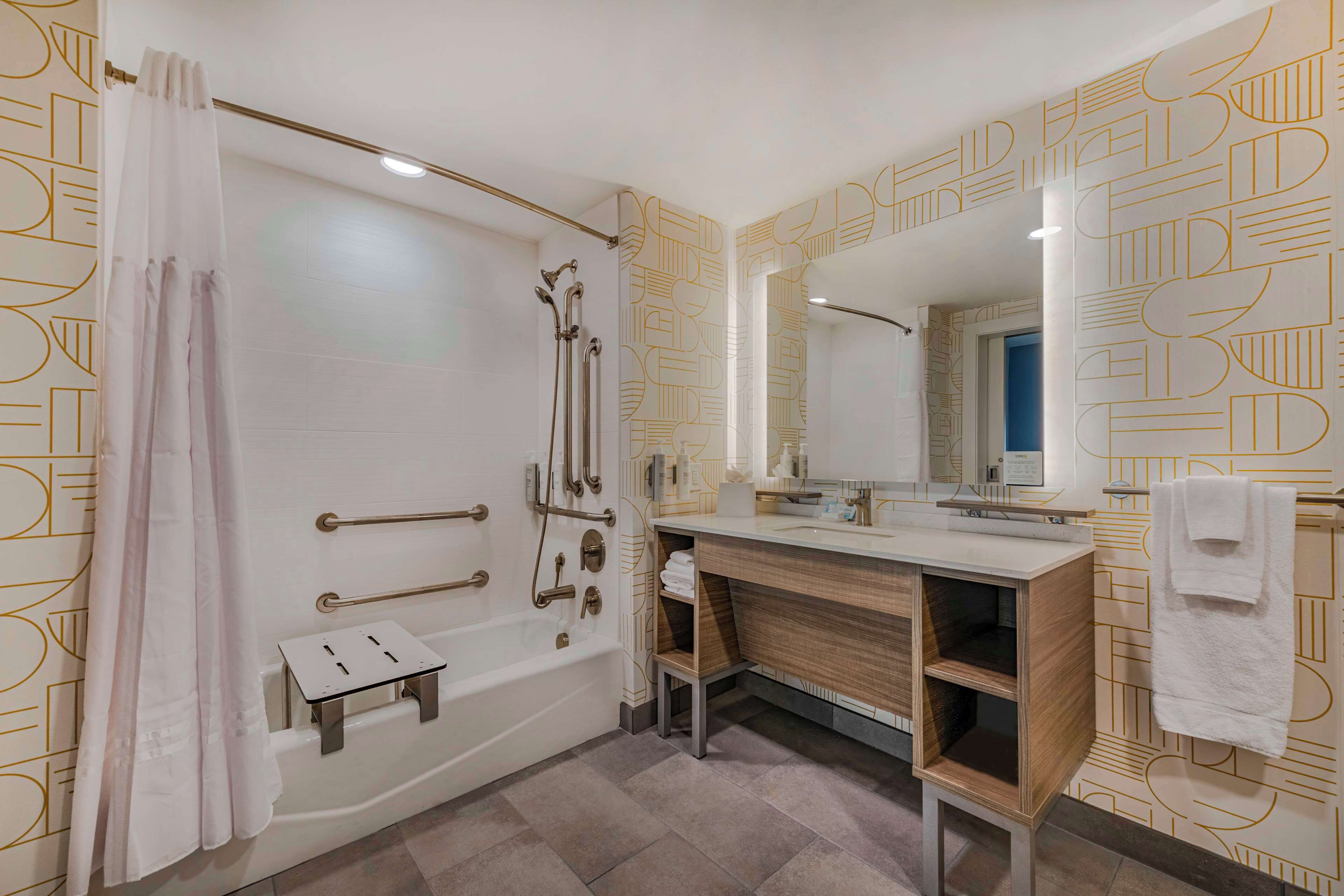A modern bathroom with a walk-in shower, grab bars, a vanity with a mirror, and a towel rack.