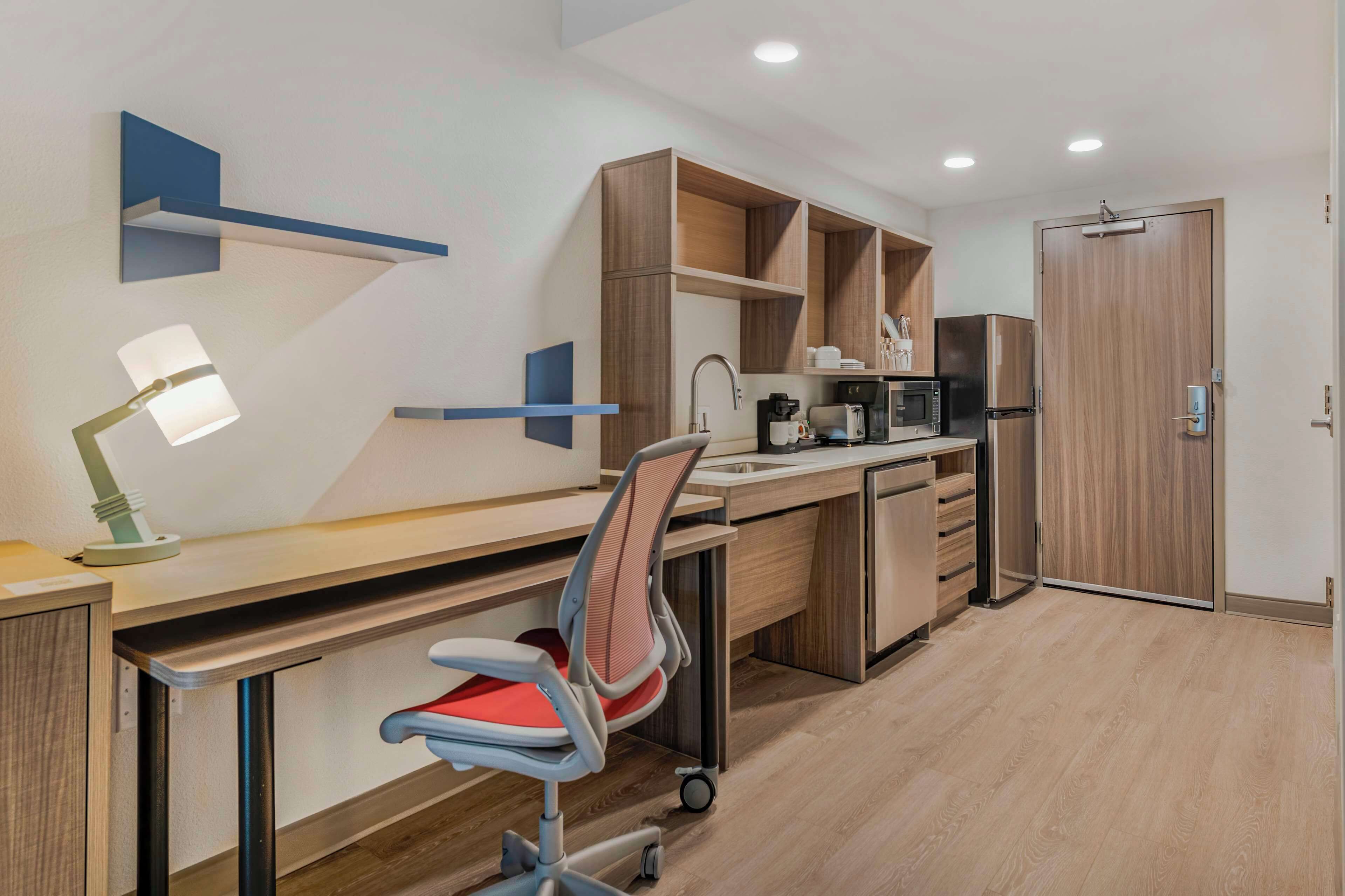 A modern kitchen with a built-in desk, a chair, a lamp, and a microwave.