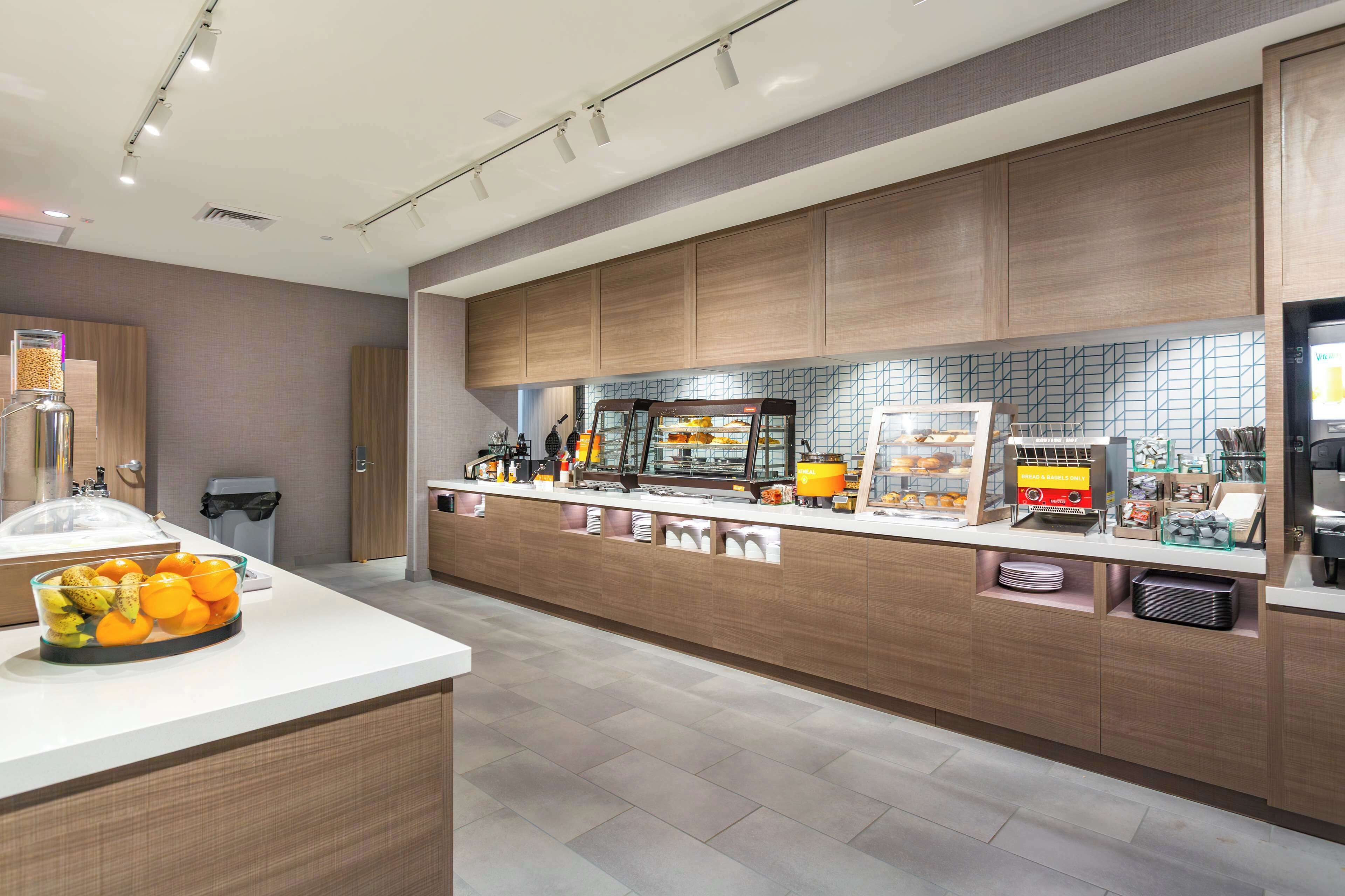 A modern kitchen area with a breakfast bar, a fruit bowl, and various food items displayed.