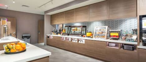 A modern kitchen area with a breakfast bar, a fruit bowl, and various food items displayed.