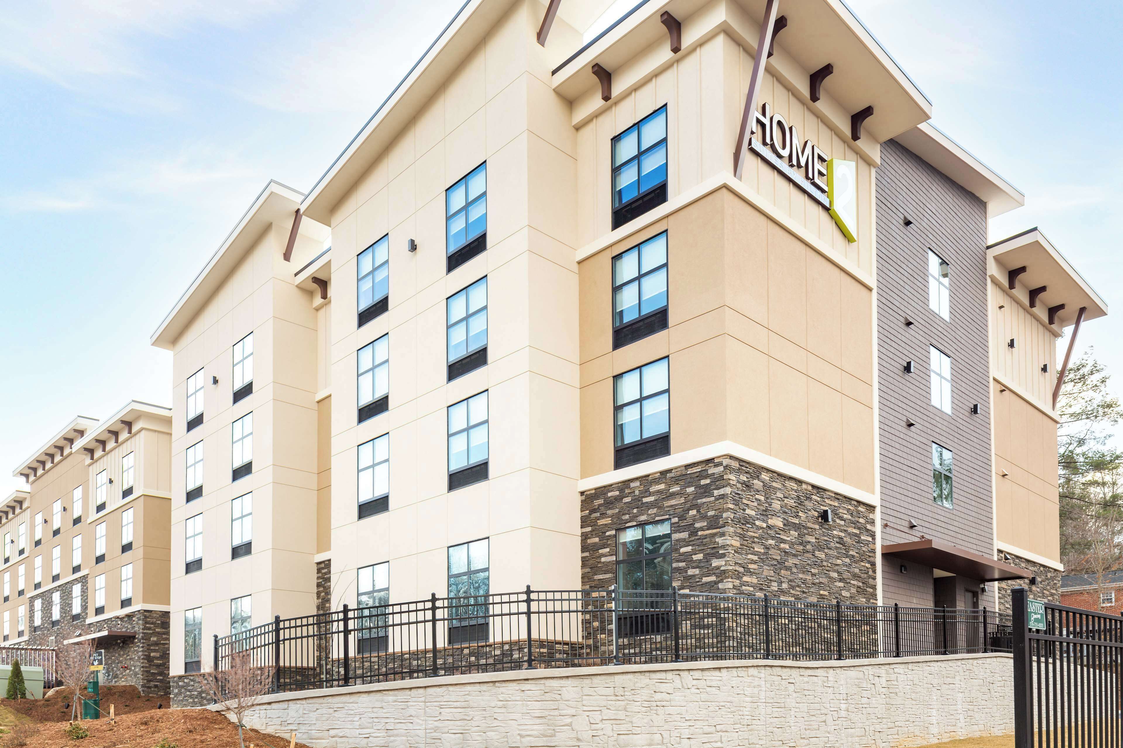 Un hotel de varios pisos con fachada color beige, detalles de piedra y un letrero que dice “HOME”.