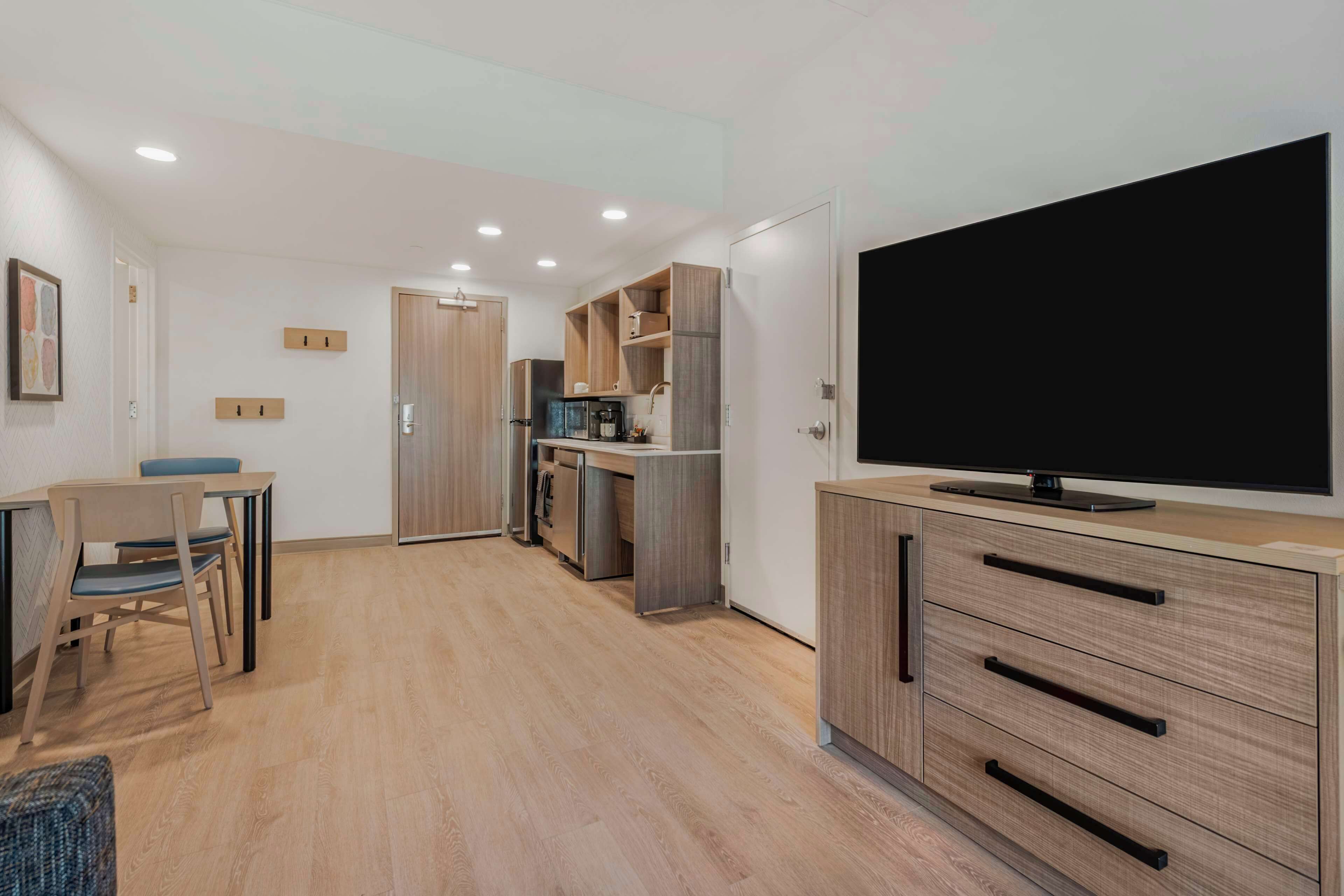 A modern kitchen with a flat-screen TV, wooden cabinets, and a dining area with a table and chairs.