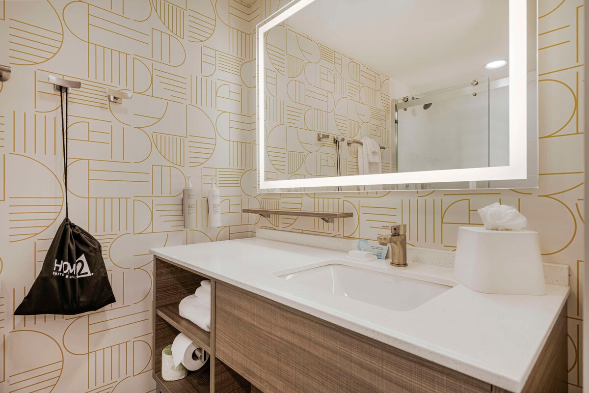 A modern bathroom with a large mirror, a white sink, and a towel rack.