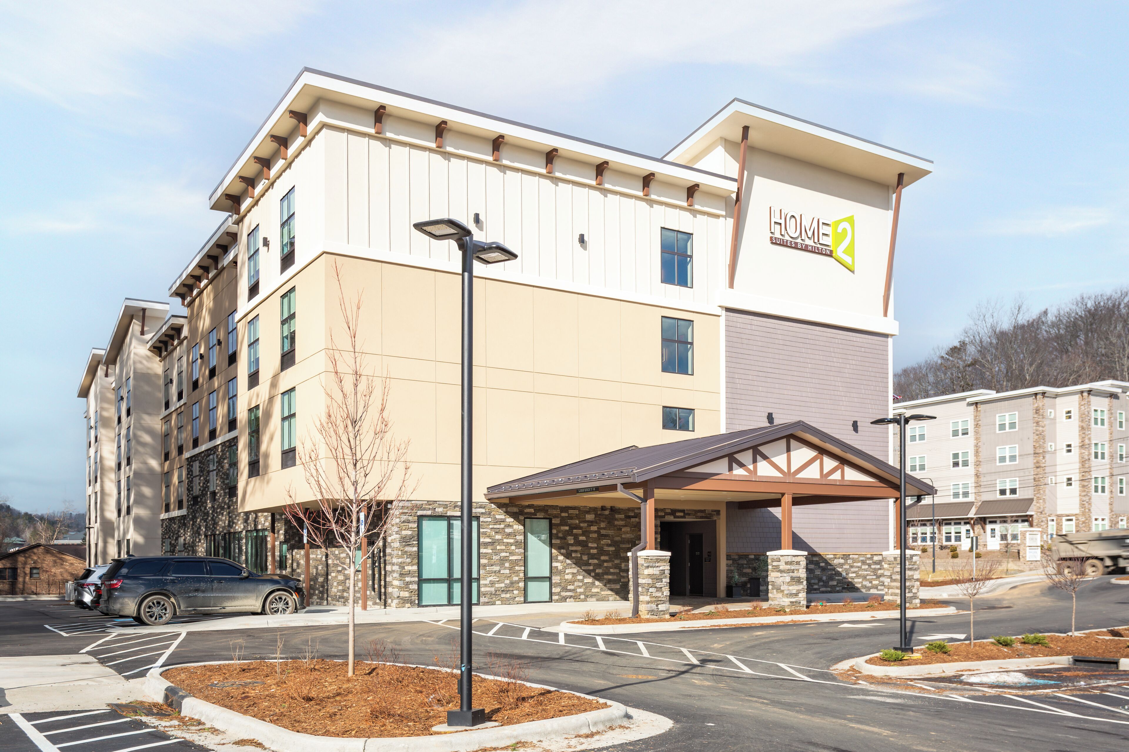 A multi-story hotel with a beige and brown exterior, a covered entrance, and a parking lot.