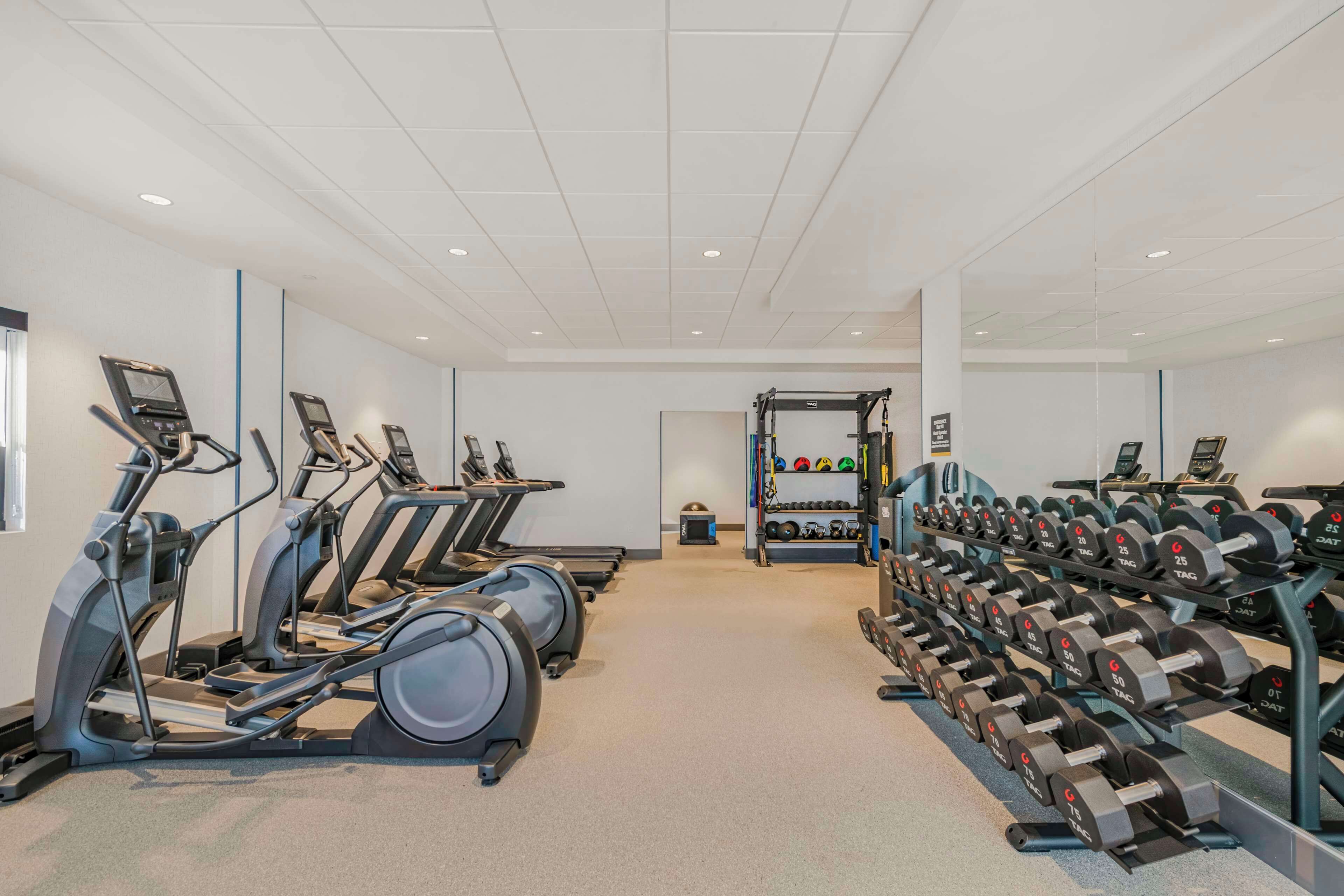 A gym with treadmills, elliptical machines, and a rack of dumbbells.