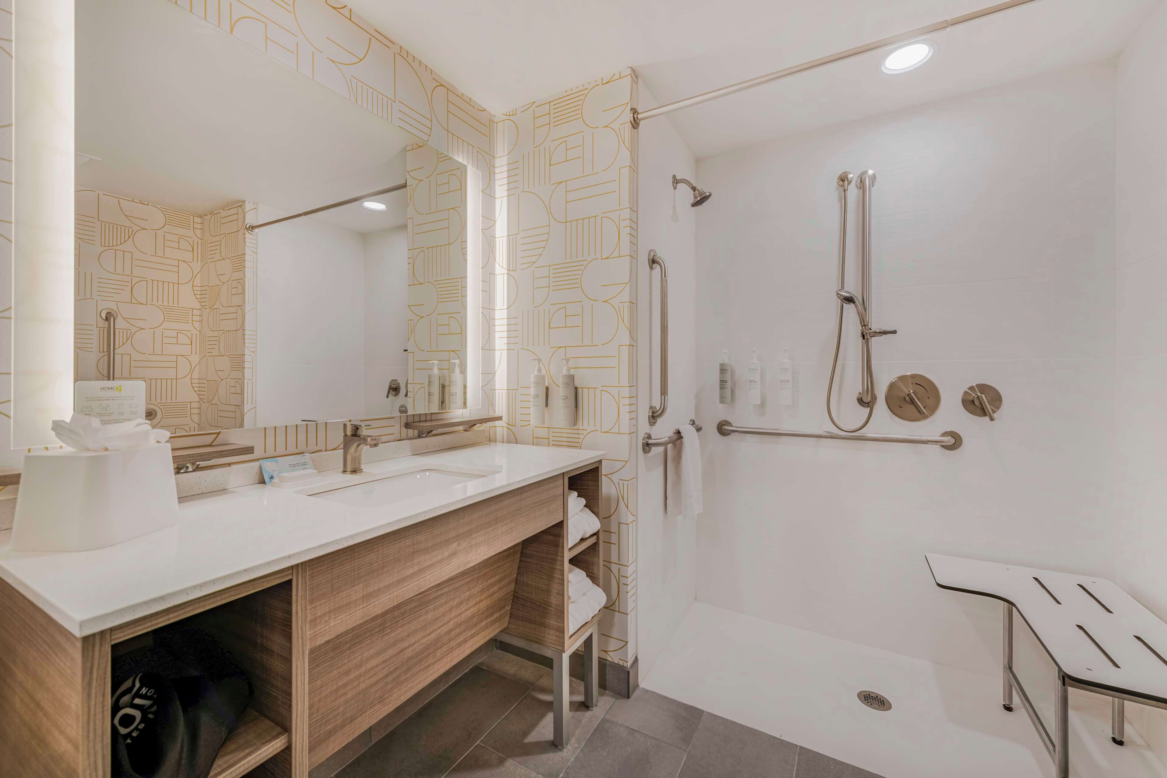 Un baño moderno con un espejo grande, dos lavamanos, una ducha con cabezal de ducha manual y un plato de ducha de cristal.