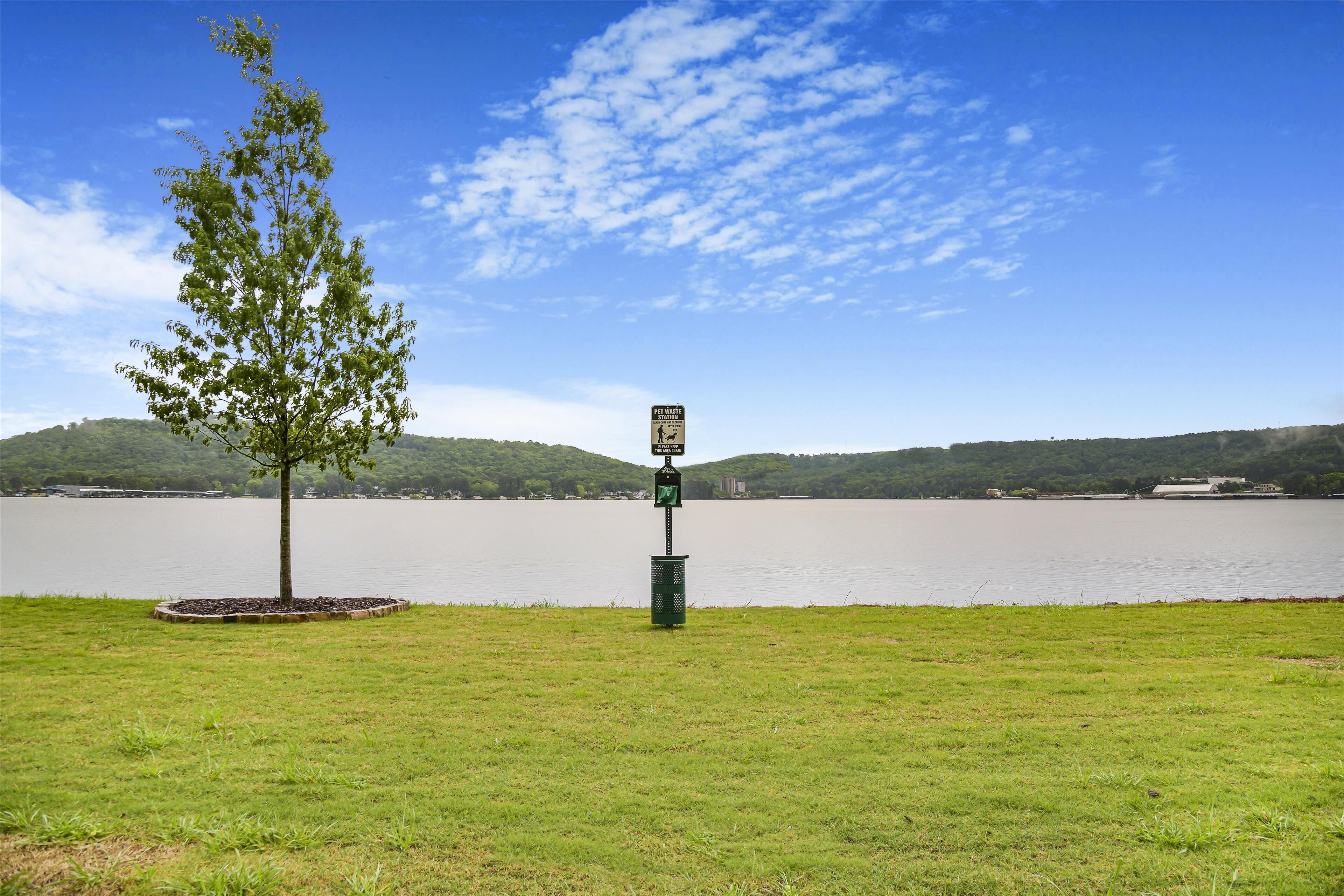 Une zone herbeuse avec un panneau indicateur et un arbre au bord d’un lac.